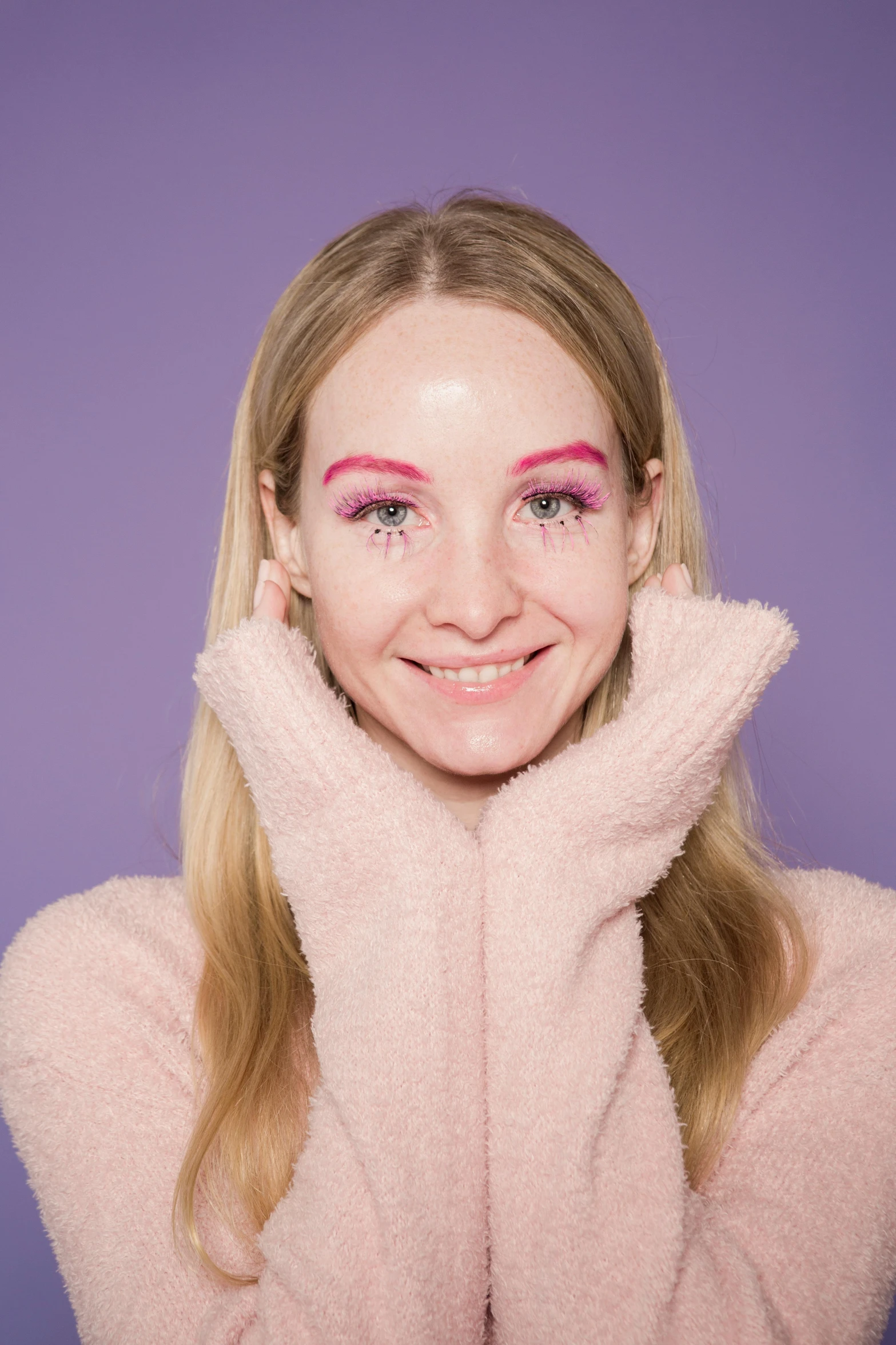 a woman in a pink sweater posing with her hands on her face, an album cover, inspired by Maud Naftel, trending on pexels, happy eyes, britt marling style 3/4, purple makeup, red contact lenses
