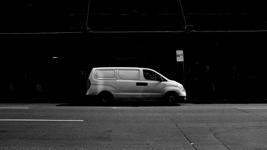 a white van parked in front of a building, a black and white photo, by Thomas Furlong, pexels contest winner, on a sidewalk of vancouver, anonymous as a car, white on black, blank