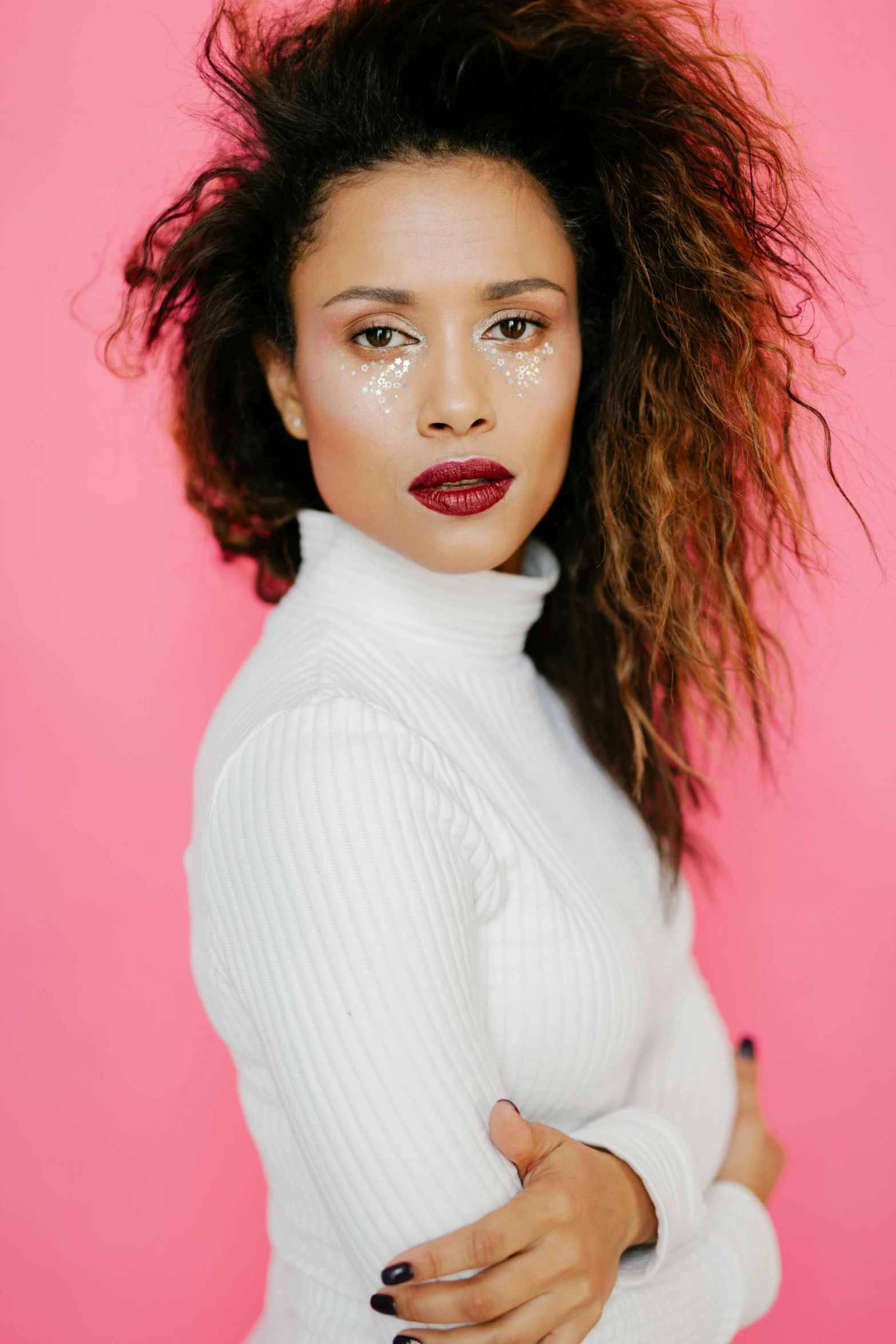 a woman with long hair standing in front of a pink background, bright red lipstick, mixed race woman, with textured hair and skin, photo from a promo shoot