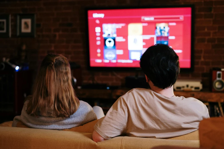 a couple of people sitting on a couch in front of a tv, pexels, red color theme, technologies, college, large screen