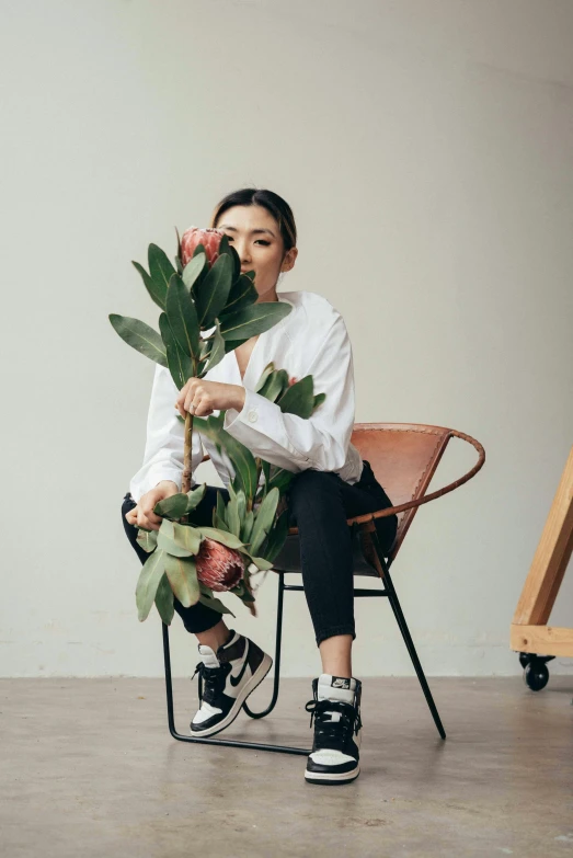 a woman sitting on a chair holding a bunch of flowers, inspired by Ruth Jên, trending on unsplash, minimalism, she is wearing streetwear, asian descent, lush gnarly plants, standing on a lotus