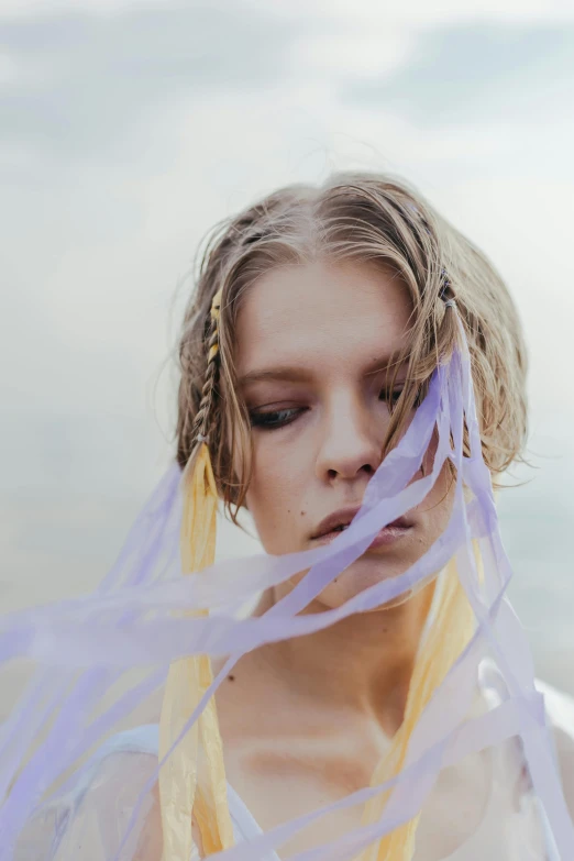 a woman standing on top of a beach next to the ocean, an album cover, inspired by Louisa Matthíasdóttir, trending on pexels, renaissance, purple ribbons, androgynous face, feathers ) wet, wavy hair yellow theme