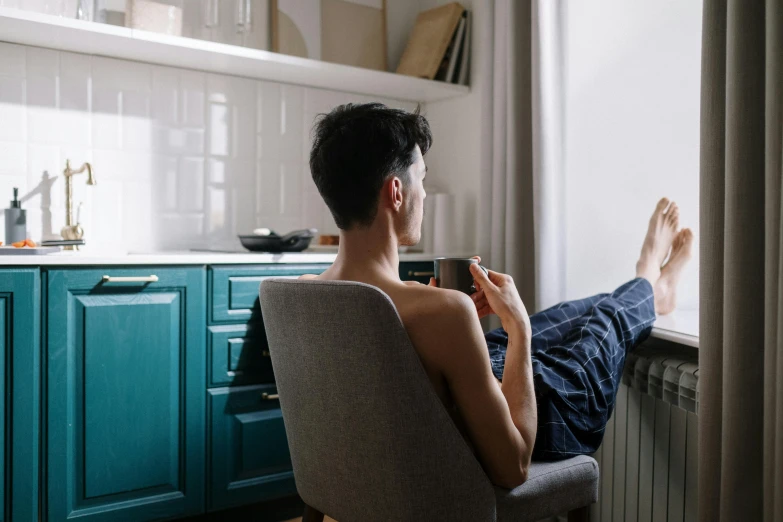 a man sitting in a chair looking out a window, trending on pexels, queer woman, studyng in bedroom, wearing only pants, having a snack