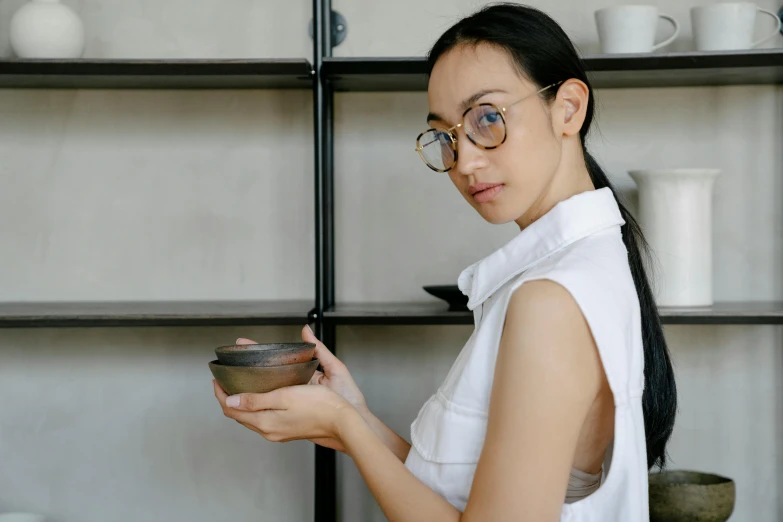 a woman standing in a kitchen holding a bowl, inspired by Kim Tschang Yeul, pexels contest winner, mingei, with black eyeglasses, avatar image, porcelain organic, japanese collection product