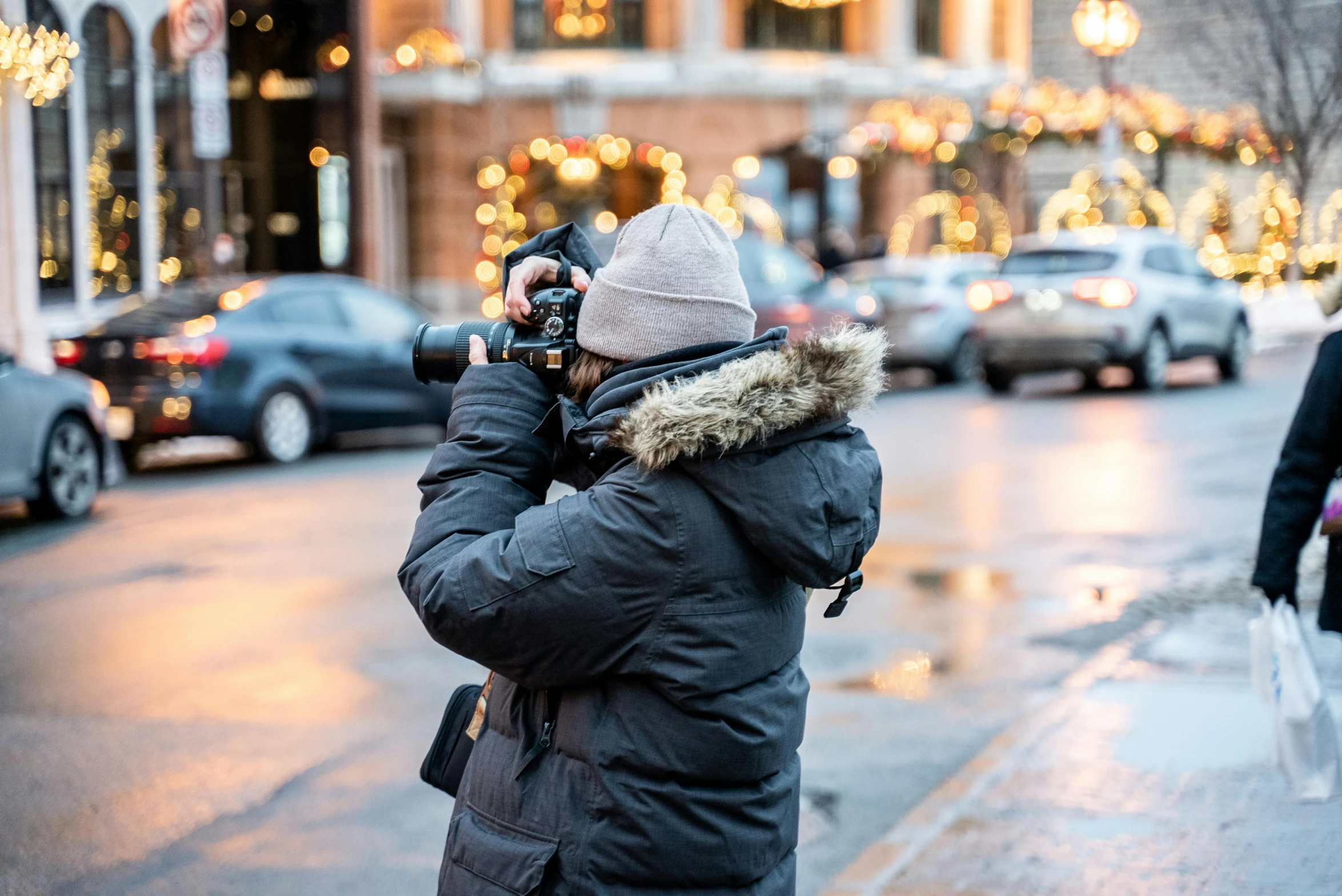 a person taking a picture on a city street, by Julia Pishtar, pexels contest winner, cold weather, telephoto vacation picture, behind the scenes photo, holiday season