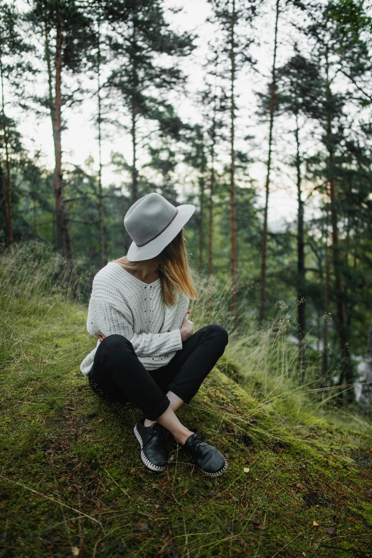 a woman sitting on top of a grass covered hill, a picture, by Anna Boch, trending on unsplash, with hat, casual modern clothing, in serene forest setting, wearing casual sweater