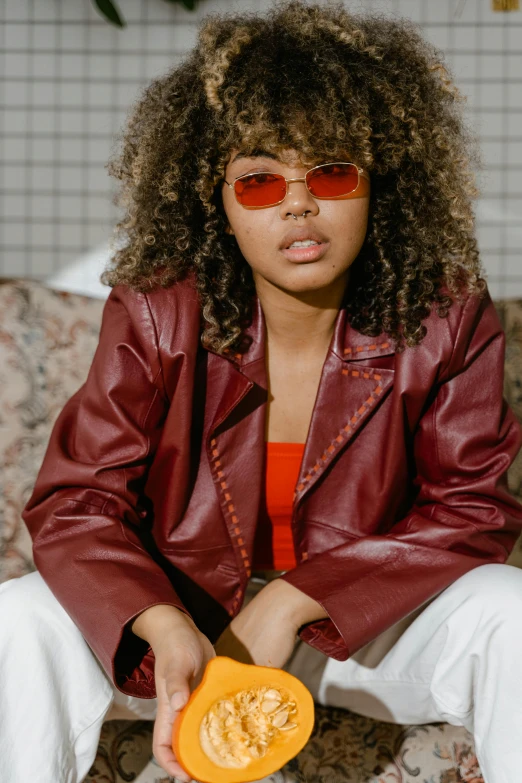 a woman sitting on a couch holding a pumpkin, an album cover, by Cosmo Alexander, trending on pexels, red leather jacket, aviators, mixed-race woman, teenager girl