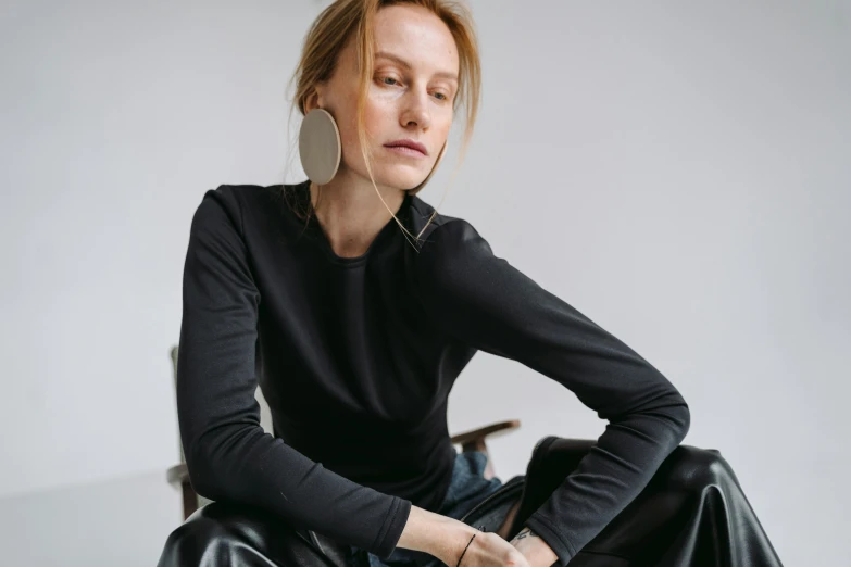 a woman sitting on a chair wearing headphones, by Nina Hamnett, trending on pexels, bauhaus, black turtle neck shirt, thin round earrings, detailed product image, shungite bangle