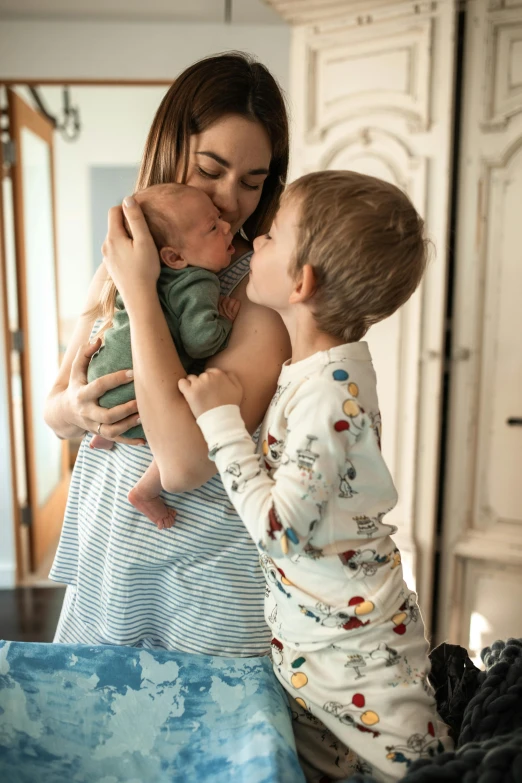 a woman holding a baby and kissing a boy, a picture, by Everett Warner, pexels contest winner, wearing pajamas, morning detail, third trimester, brunette