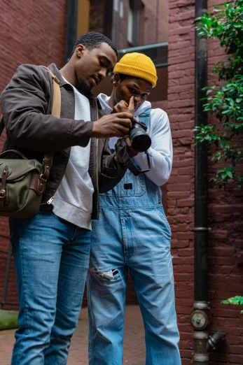 a couple of men standing next to each other on a sidewalk, inspired by Gordon Parks, trending on pexels, holding a camera, wearing overalls, ( ( theatrical ) ), brooklyn
