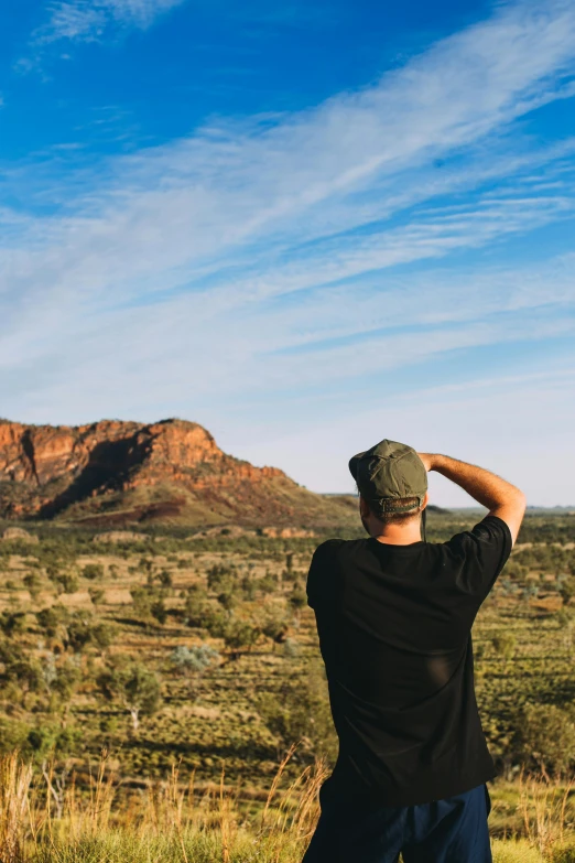 a man standing on top of a lush green field, a picture, inspired by Albert Namatjira, unsplash contest winner, overlooking martian landscape, back of head, shot from roofline, empty remote wilderness