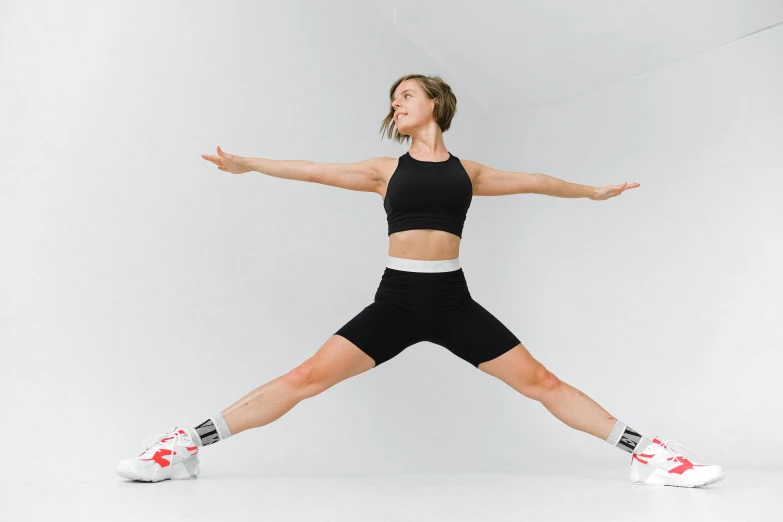 a woman in a black top and black shorts doing a yoga pose, in front of white back drop, wearing kneesocks, wearing a crop top, weightlessness