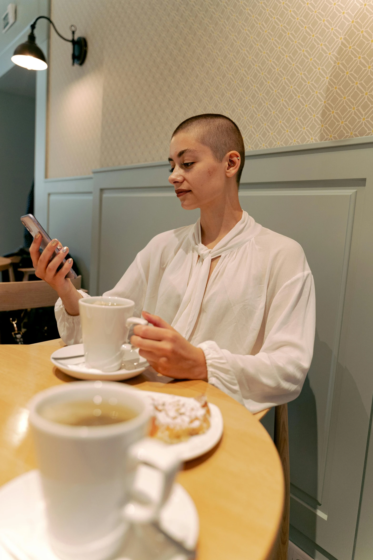 a man sitting at a table with a cup of coffee, buzz cut, checking her phone, nanae kawahara, sleek white