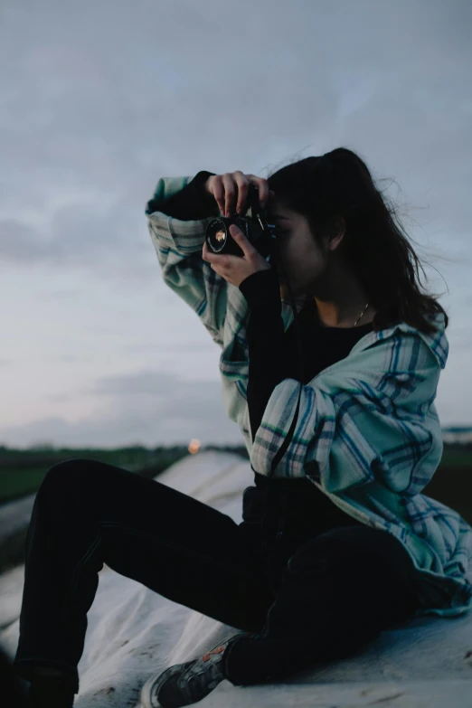 a woman sitting on a wall taking a picture with a camera, a picture, trending on unsplash, dusk setting, texture, casual pose, focus on the sky