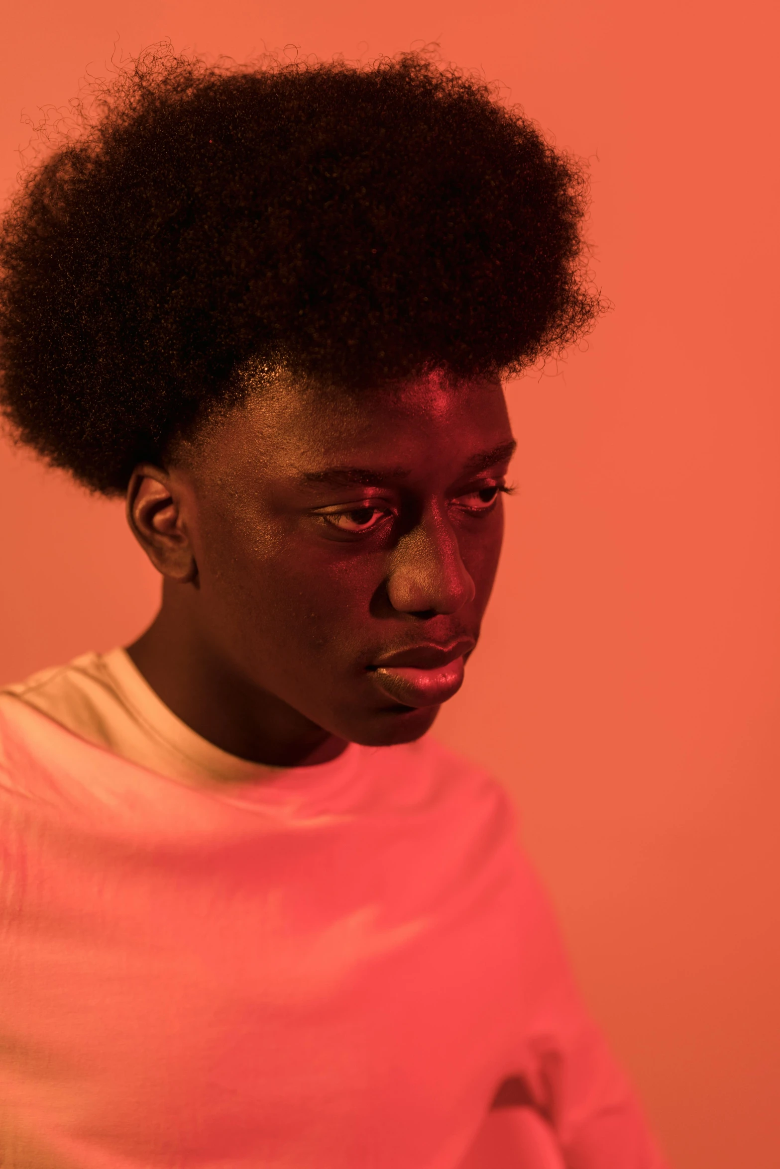 a woman standing in front of a pink wall, an album cover, pexels contest winner, hyperrealism, black man with afro hair, soft red lights, looks sad and solemn, portrait androgynous girl