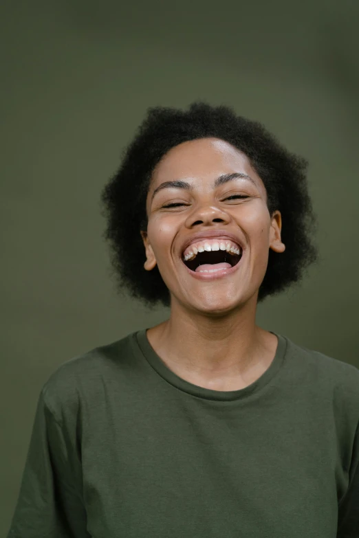 a woman laughing in front of a green background, pexels contest winner, black young woman, plain background, happy with his mouth open, promo image