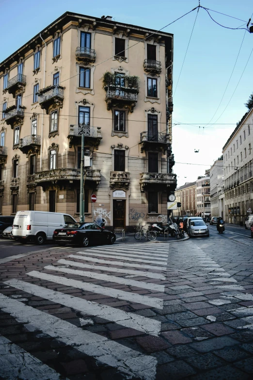 a group of cars driving down a street next to tall buildings, inspired by Gianfredo Camesi, pexels contest winner, renaissance, palermo city street, crosswalk, cobblestones, seen from outside