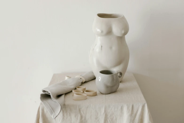 a white vase sitting on top of a table, a marble sculpture, inspired by Sarah Lucas, process art, white loincloth, with a white mug, full figure, ecru cloth