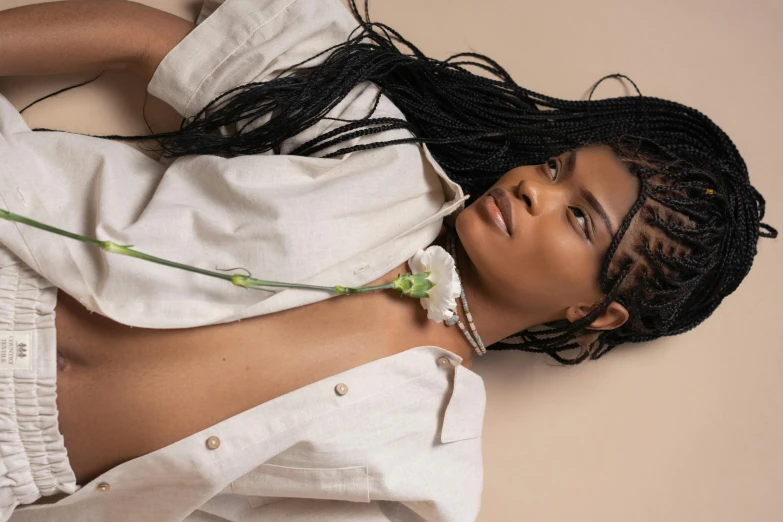 a woman laying down with a flower in her hand, by Cosmo Alexander, trending on pexels, afrofuturism, long black braided hair, on a pale background, wearing jewellery, androgynous person