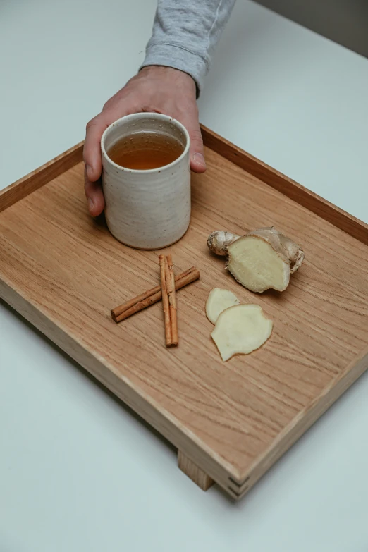 a person holding a cup of tea on a wooden tray, inspired by Kanō Shōsenin, renaissance, cinnamon, detailed product image, recipe, ginger