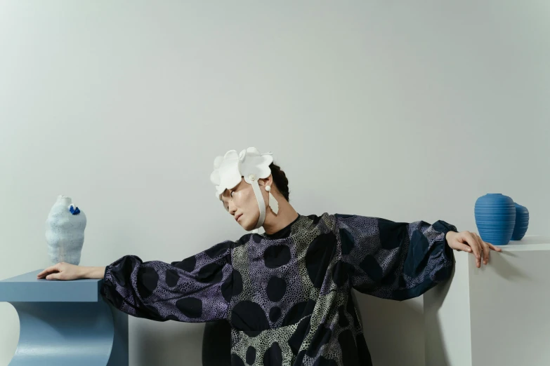 a woman standing next to a table with a bird on it, inspired by Gao Cen, unsplash, shin hanga, fashion studio lighting, with shoulder pads, issey miyake, wearing a flower headpiece