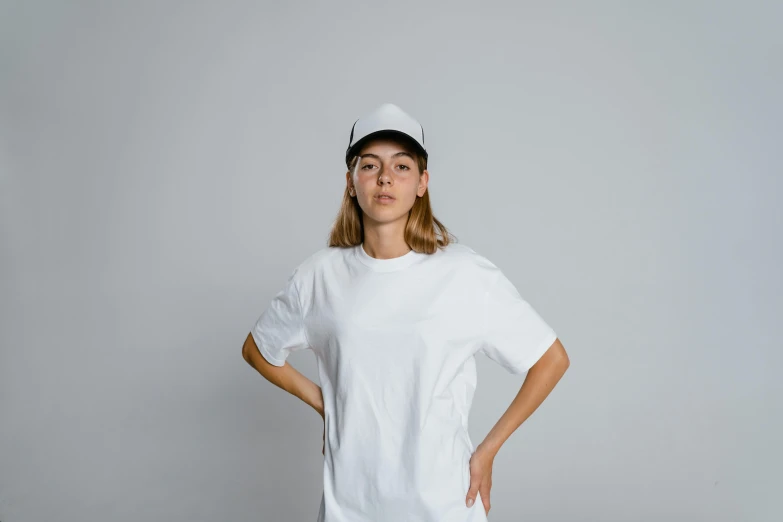 a woman in a white t - shirt is standing with her hands on her hips, pexels contest winner, baseball cap, trending on r/streetwear, blank background, genderless