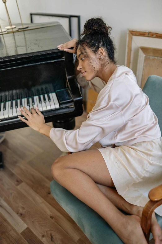 a woman sitting on a couch playing a piano, inspired by Elsa Bleda, pexels contest winner, renaissance, black young woman, battered, on a pale background, sitting on chair