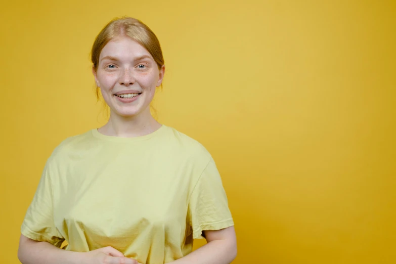a young woman standing in front of a yellow wall, pexels contest winner, realism, greta thunberg smiling, hr ginger, nursing, male teenager