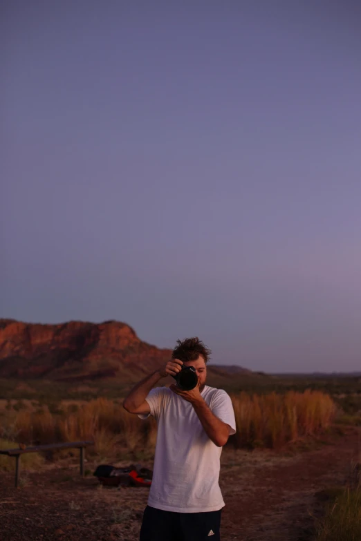 a man standing on a dirt road taking a picture, a picture, by Lee Loughridge, at twilight, in between a gorge, outback, dylan kowalsk