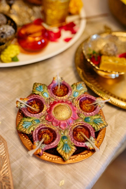 a close up of plates of food on a table, hindu ornaments, floating candles, gold flaked flowers, and