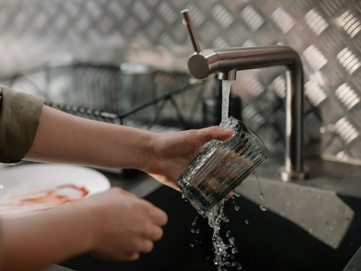 a person washing their hands under a faucet, by Daniel Lieske, pexels contest winner, mixing drinks, family friendly, transparent, stainless steel