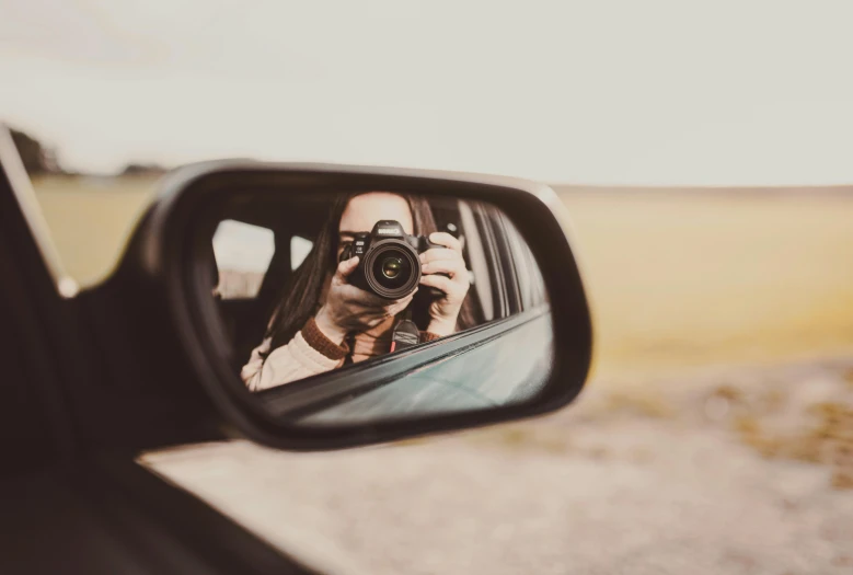 a woman taking a picture of herself in a rear view mirror, a picture, inspired by Elsa Bleda, pexels contest winner, holding a dslr camera, lovingly looking at camera, vehicle, mid body shot