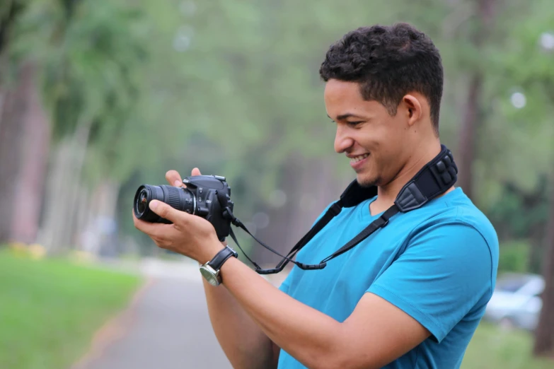 a man in a blue shirt holding a camera, a picture, pexels contest winner, ariel perez, smiling for the camera, avatar image, outdoor photo