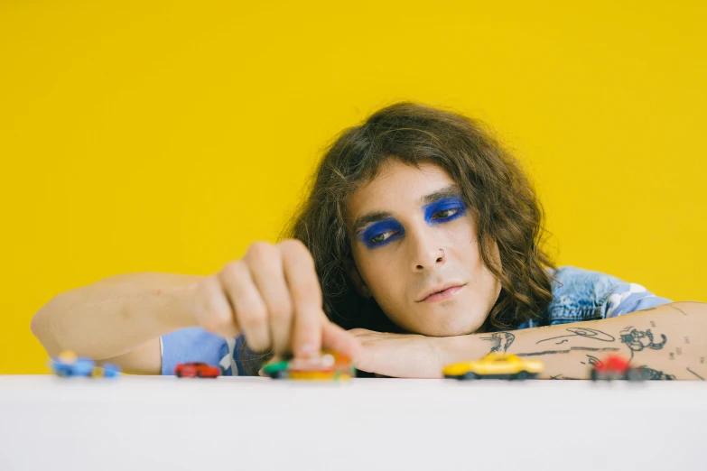 a man sitting at a table with legos in front of him, an album cover, by Winona Nelson, trending on pexels, mullet, robert sheehan, blue and yellow, cars