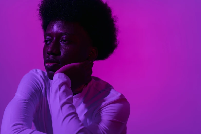 a man sitting in front of a purple background, afro, pink lighting, looking to his left, monochromatic