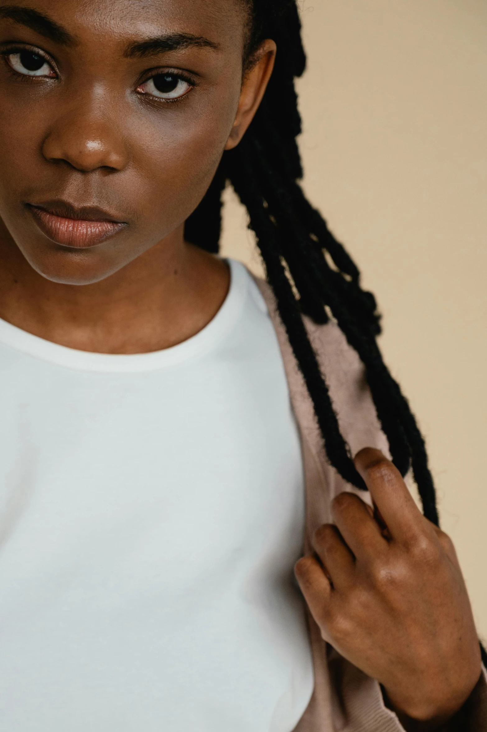 a close up of a person with long hair, by Louisa Puller, trending on pexels, afrofuturism, waist reaching ponytail, white tank top, tonal topstitching, plain background