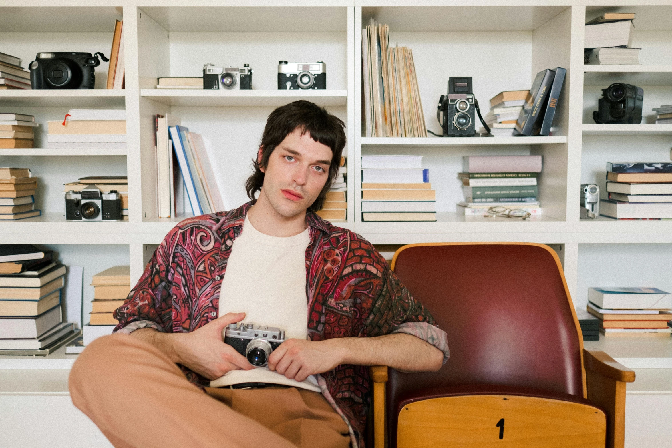 a man sitting in a chair reading a book, an album cover, by Nina Hamnett, pexels, young handsome pale roma, adam ondra, paisley, casually dressed