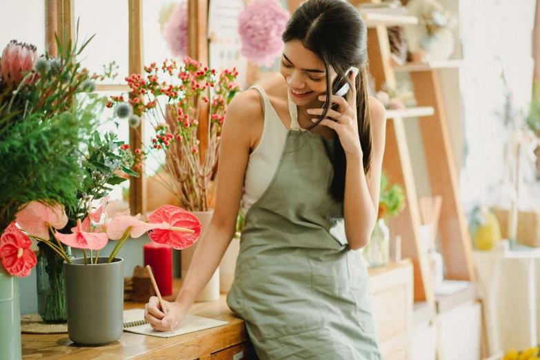 a woman talking on a cell phone in a flower shop, trending on pexels, artist wearing overalls, on a desk, asian women, attractive photo