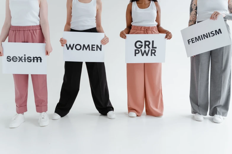 a group of women standing next to each other holding signs, by Arabella Rankin, trending on pexels, wearing pants, on grey background, !female, female gigachad