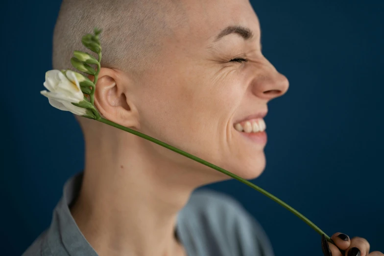 a close up of a person with a flower in their hair, inspired by Elsie Few, pexels contest winner, antipodeans, shaved head, head bent back in laughter, portrait of tall, long crooked nose