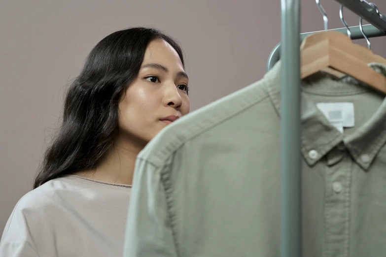 a woman standing in front of a rack of clothes, inspired by Fei Danxu, trending on pexels, hyperrealism, close up shot from the side, avatar image, pondering, brown clothes