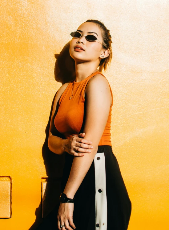 a woman standing in front of a yellow wall, trending on pexels, orange and black, wearing : tanktop, with sunglass, cindy avelino