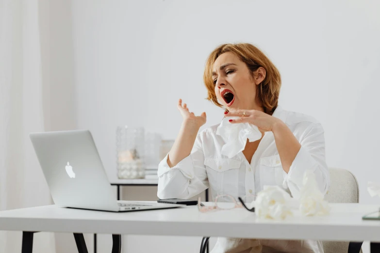 a woman sitting at a table in front of a laptop, trending on pexels, yawning, drinking cough syrup, avatar image, wearing a white blouse