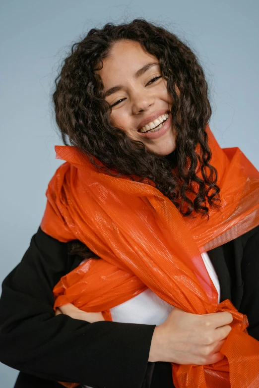 a woman wearing an orange scarf and black jacket, an album cover, inspired by Christo, pexels contest winner, wearing a plastic garbage bag, smiling young woman, karla ortiz, hailee steinfeld