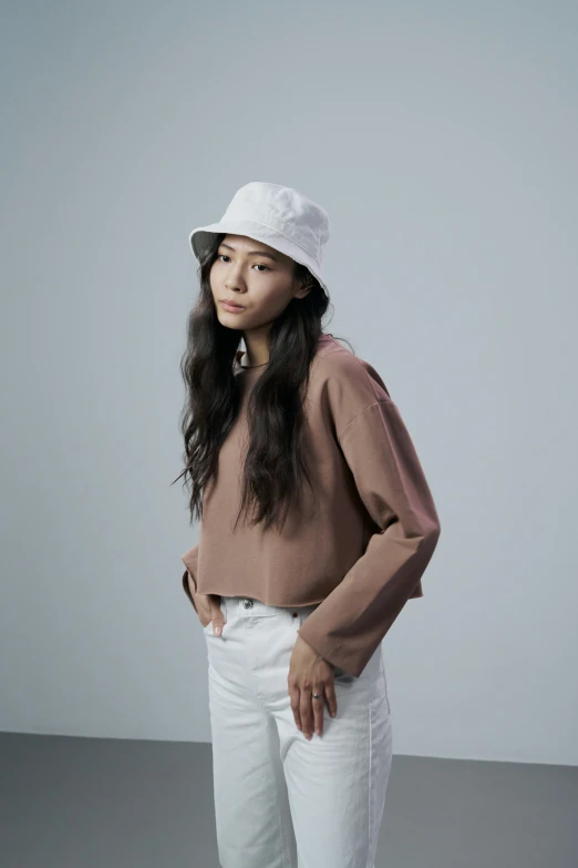 a woman standing with her hands in her pockets, by Simon Gaon, unsplash, minimalism, wears a destroyed hat, gradient brown to white, jaeyeon nam, wearing a cropped top