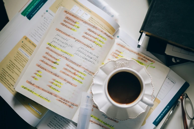 a cup of coffee sitting on top of a pile of papers, trending on pexels, analytical art, biology textbook page, random english words, background image, studying in a brightly lit room