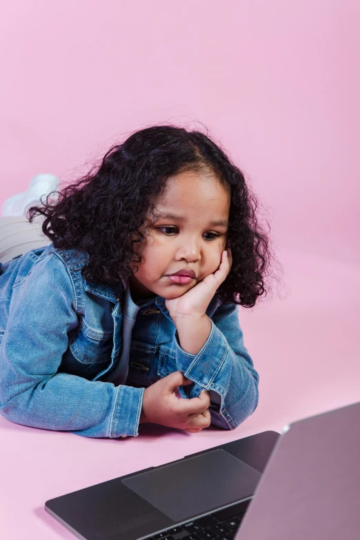 a little girl laying on the floor next to a laptop, a cartoon, trending on pexels, mixed race, disappointed, pink hue, hand on her chin