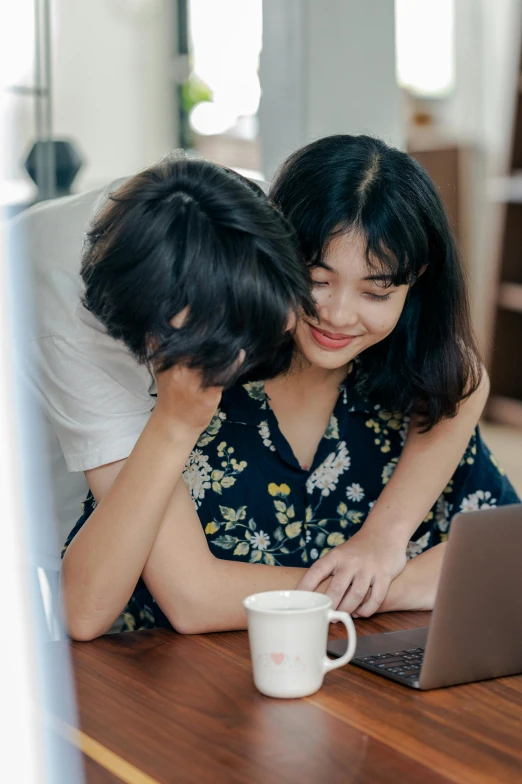 a couple of people sitting at a table with a laptop, by Zeen Chin, pexels contest winner, happening, hugging, young asian girl, with a white mug, romantic lead