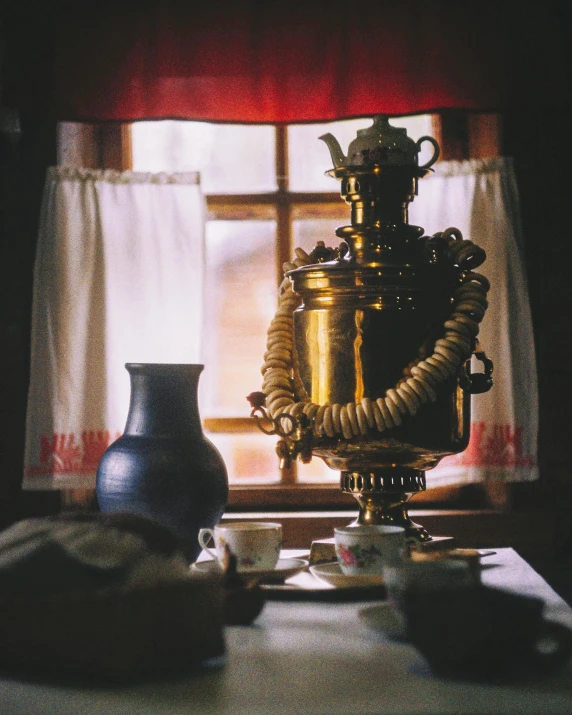 a vase sitting on top of a table next to a window, ancient coffee machine, kalevala, traditional clothes, gold