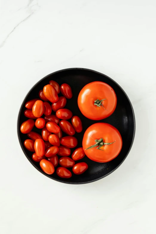 a black bowl filled with tomatoes on top of a white table, product image, hegre, moderate colors, petite